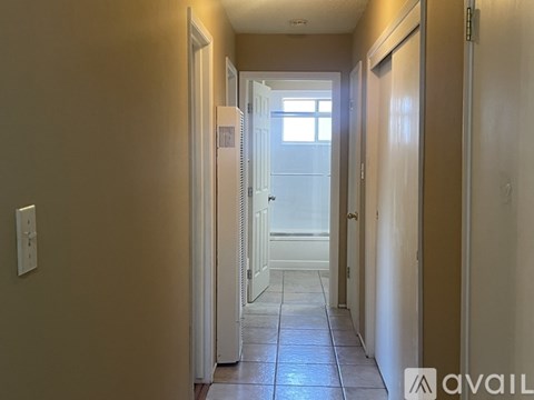 A hallway with a light switch on the wall and a door at the end.