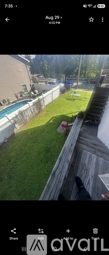 A person is standing on a wooden deck overlooking a backyard with a pool and a fence.