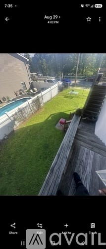 A person is standing on a wooden deck overlooking a backyard with a pool and a fence.