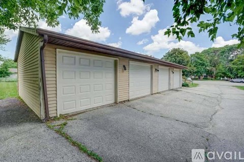A tan garage with a brown roof is surrounded by a concrete driveway.