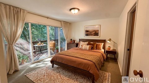 A bedroom with a large bed and a view of a backyard through the window.