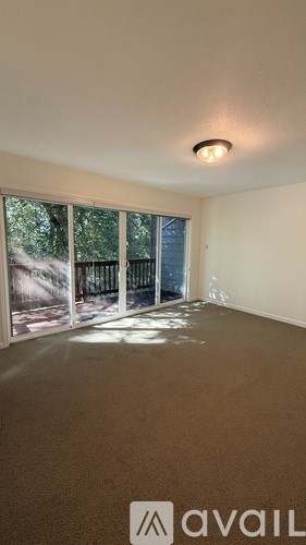 A room with a carpeted floor and a window with a view of trees and a fence.