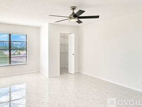 A room with a ceiling fan and a large window with a view of a fence and trees.