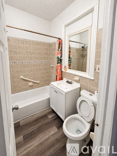 A small white toilet is in a bathroom with a white tub and a window.