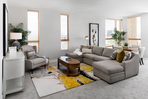 A living room with a grey sofa, a white armchair, a wooden coffee table, and a rug with a yellow design.