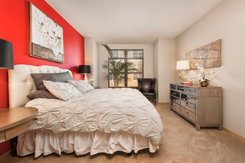 A bedroom with a large bed and a red accent wall.