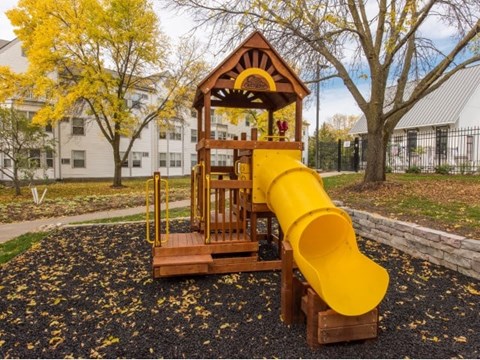 A playground with a yellow slide and a wooden structure.