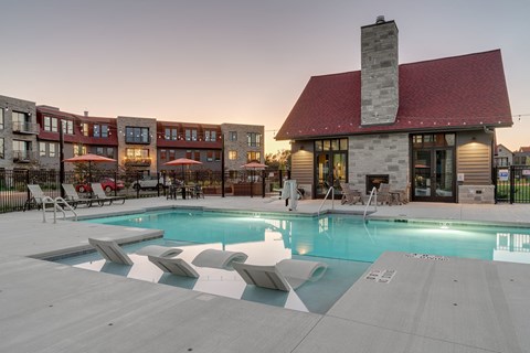 A swimming pool with sun loungers in front of a building with a red roof.