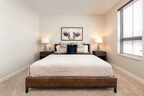 A bedroom with a bed, two lamps, and a picture on the wall.