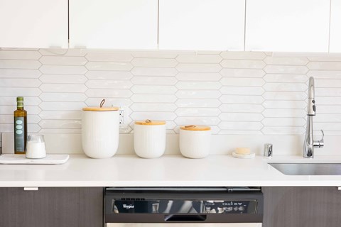 A kitchen counter with a bottle, a bowl, a pot, and a container on it.