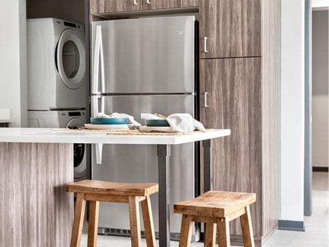 A modern kitchen with a stainless steel refrigerator and wooden stools.