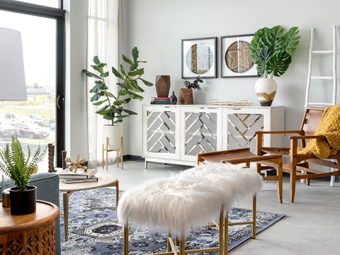 A living room with a white furry ottoman and a wooden table with a plant on it.