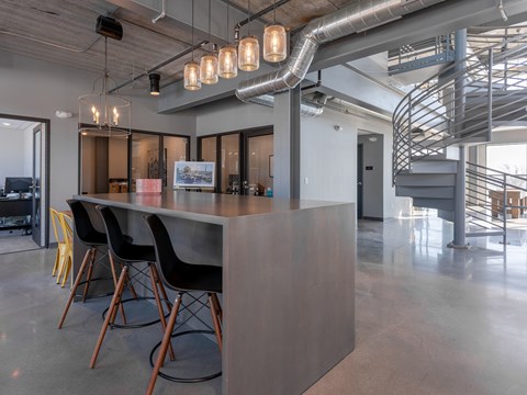 A modern office space with a long grey counter and black chairs.