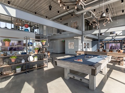 A pool table is in the middle of a room with lots of shelves and potted plants.