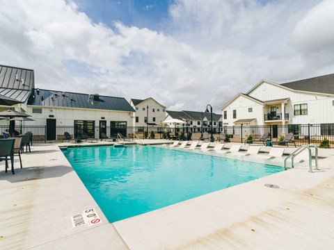 A large swimming pool in front of a building with a poolside lounge area.