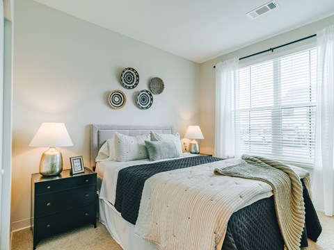 A bedroom with a large bed, a black dresser, and a window with blinds.