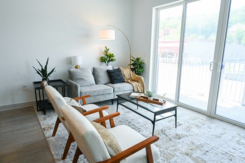 A living room with a grey couch, a wooden chair, and a glass table.