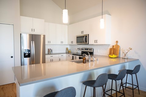 A modern kitchen with a stainless steel refrigerator, a microwave above the stove, and a bar area with three chairs.