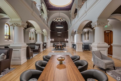 A large wooden table is surrounded by leather chairs in a spacious room with arched ceilings and a chandelier.