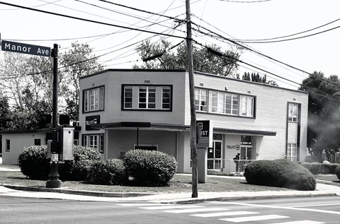 A black and white image of a street corner with a building and a street sign.