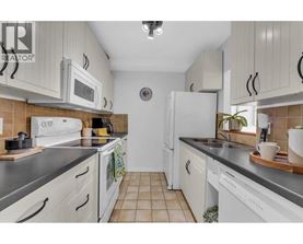 A kitchen with white cabinets and appliances, a tiled floor, and a clock on the wall.