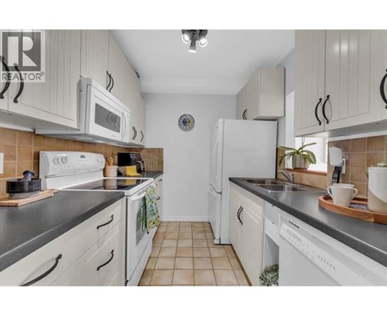 A kitchen with white cabinets and appliances, a tiled floor, and a clock on the wall.