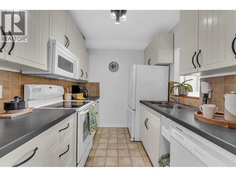 A kitchen with white cabinets and appliances, a tiled floor, and a clock on the wall.
