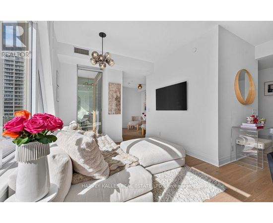 A living room with a white couch and a vase of pink roses.