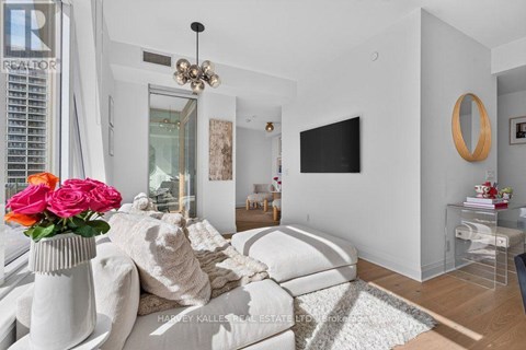 A living room with a white couch and a vase of pink roses.
