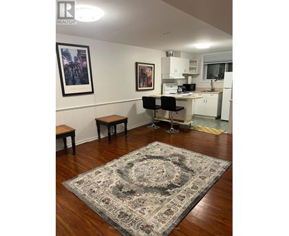 A room with a rug on the floor and a kitchen area in the background.