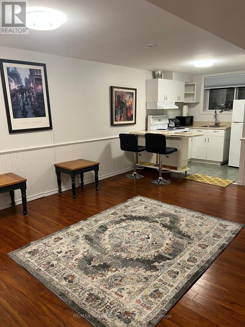 A room with a rug on the floor and a kitchen area in the background.