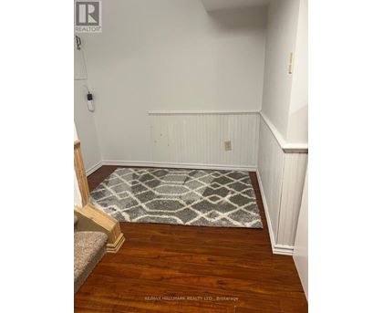 A hallway with a rug on the floor and a wooden staircase on the left.
