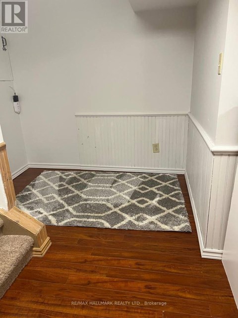 A hallway with a rug on the floor and a wooden staircase on the left.