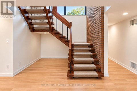 A wooden staircase with a beige carpeted runner leads up to a bright room with white walls.