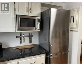 A kitchen with a stainless steel refrigerator and microwave above a granite countertop.