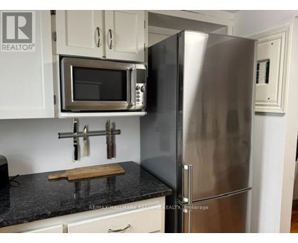 A kitchen with a stainless steel refrigerator and microwave above a granite countertop.