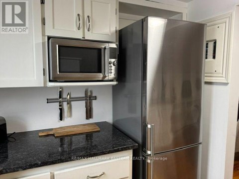 A kitchen with a stainless steel refrigerator and microwave above a granite countertop.