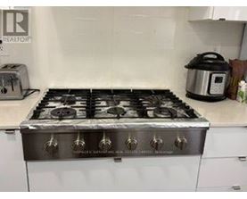 A silver gas stove with six burners is in a kitchen.