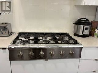 A silver gas stove with six burners is in a kitchen.