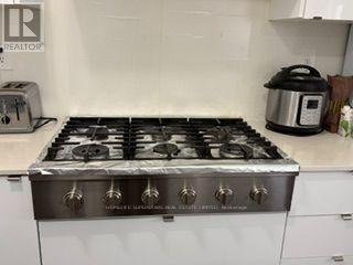 A silver gas stove with six burners is in a kitchen.
