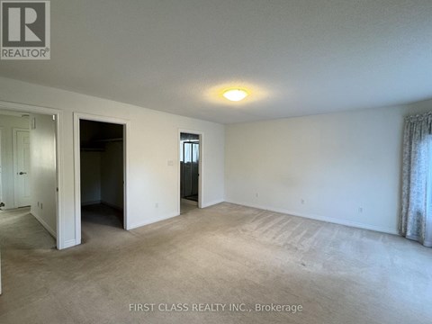 A large empty room with a carpeted floor and a window with curtains.