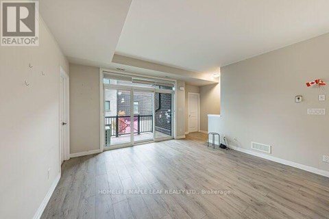 A spacious room with wooden flooring and a sliding glass door leading to a balcony.