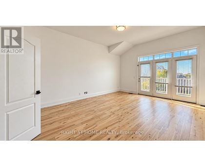 A room with wooden floors and white walls, with a door on the left and a window with blinds on the right.
