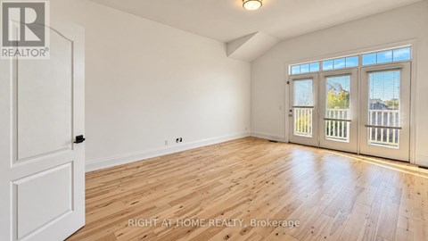 A room with wooden floors and white walls, with a door on the left and a window with blinds on the right.