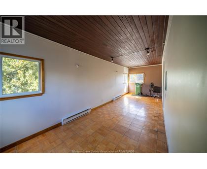 A room with a wooden ceiling and floor, a window, and a green trash can.