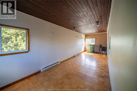 A room with a wooden ceiling and floor, a window, and a green trash can.