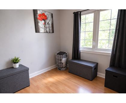 A room with a grey ottoman, a black ottoman, and a painting of a red flower on the wall.