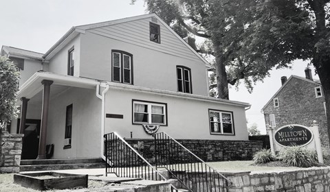 A black and white image of a house with a sign that says Millown Apartments.