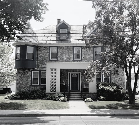 A black and white photo of a house with a stone facade and a large front porch.