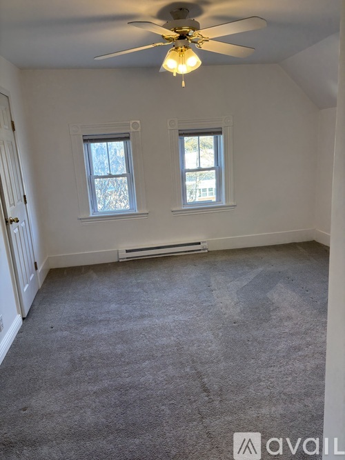 A room with a carpeted floor, a ceiling fan, and two windows.